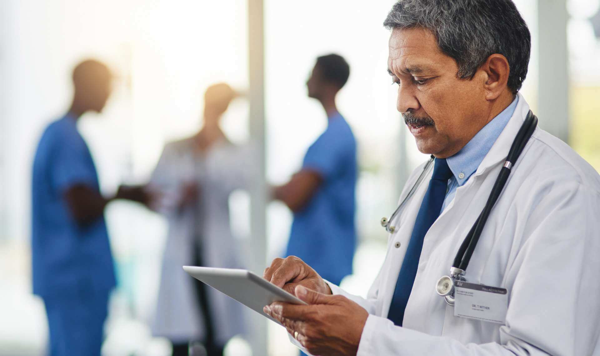 Doctor looking at a tablet while other doctors talk